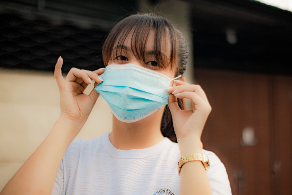 young woman wearing a surgical mask with her hands adjusting the mask on her face