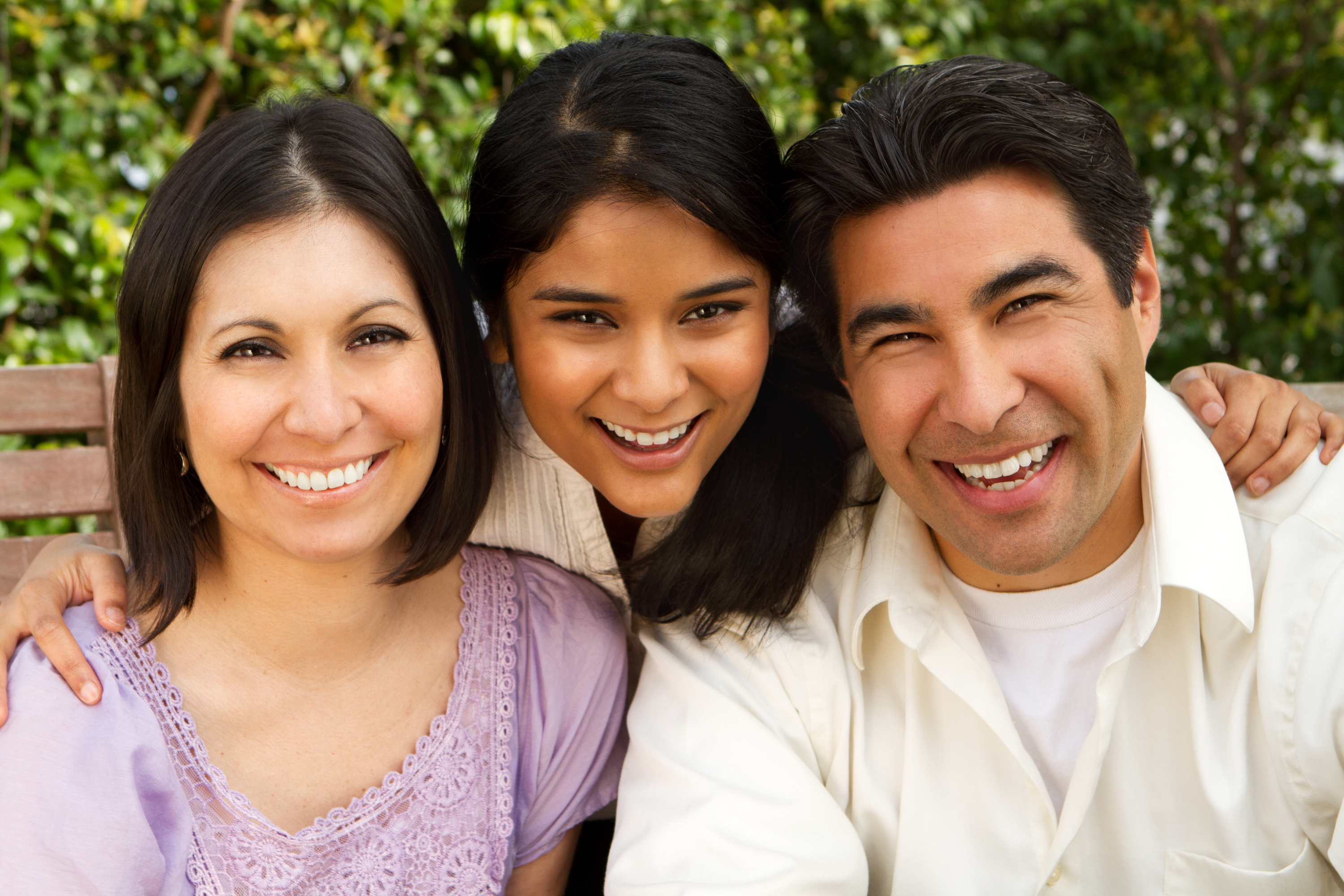 Испанская семья из трех человек улыбается на скамейке